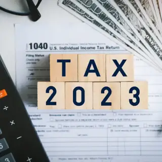 The words "Tax 2023" in little blocks sitting on top of tax forms and a calculator.