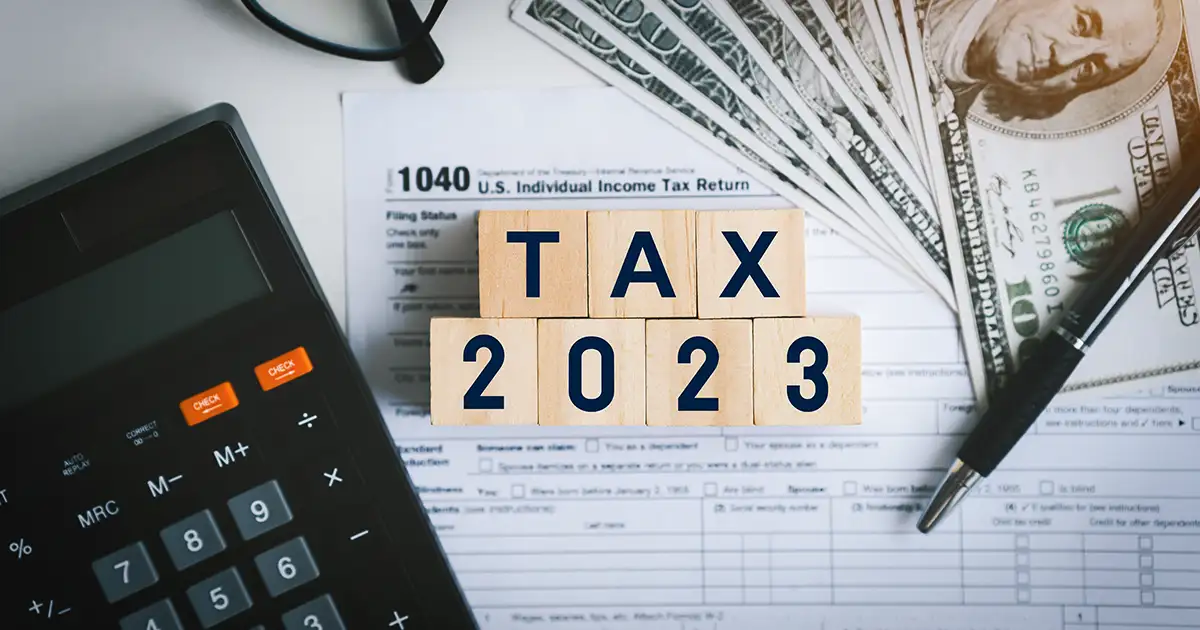 The words "Tax 2023" in little blocks sitting on top of tax forms and a calculator.