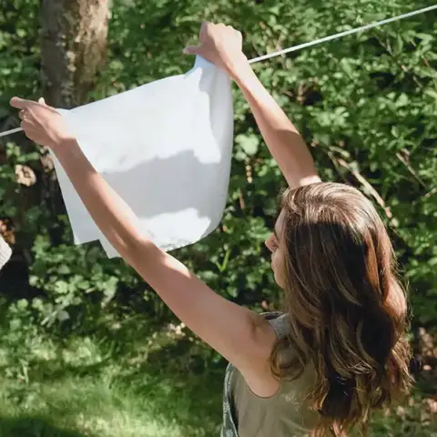 A woman hangs linens on the outdoor clothes line to dry in the sun.