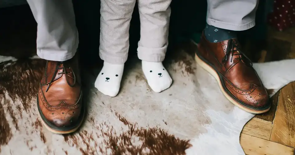 A man in his shoes, standing with his child in socks.