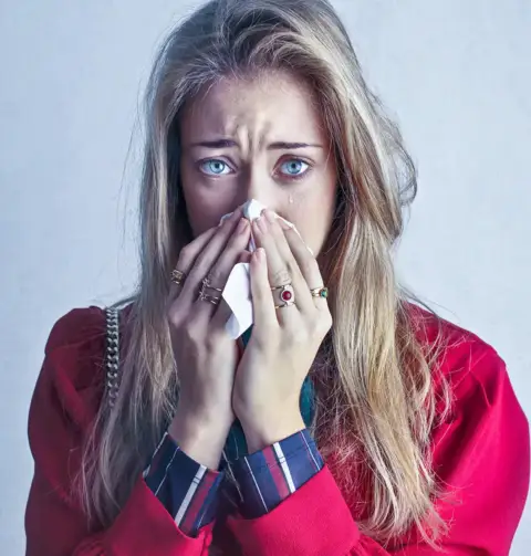 A woman suffering from seasonal allergies blows he nose into a tissue.