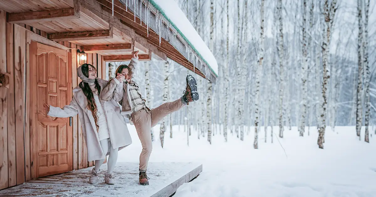 Couple laughing together as they stand on an icy porch in the middle of winter.