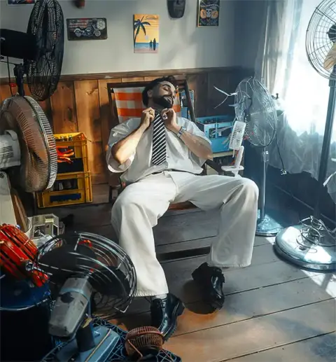 Man sits in front of multiple fans and loosens his tie, dying in the heat.