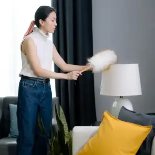 A woman uses a feather duster to clean dust from a lampshade inside her Texas home.