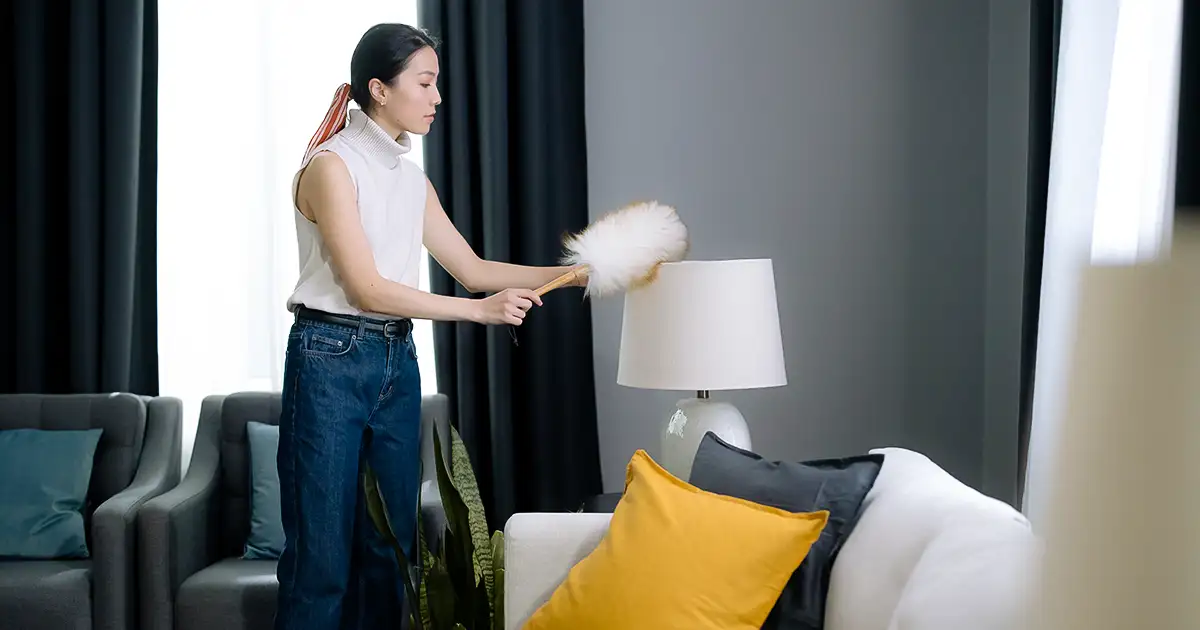 A woman uses a feather duster to clean dust from a lampshade inside her Texas home.